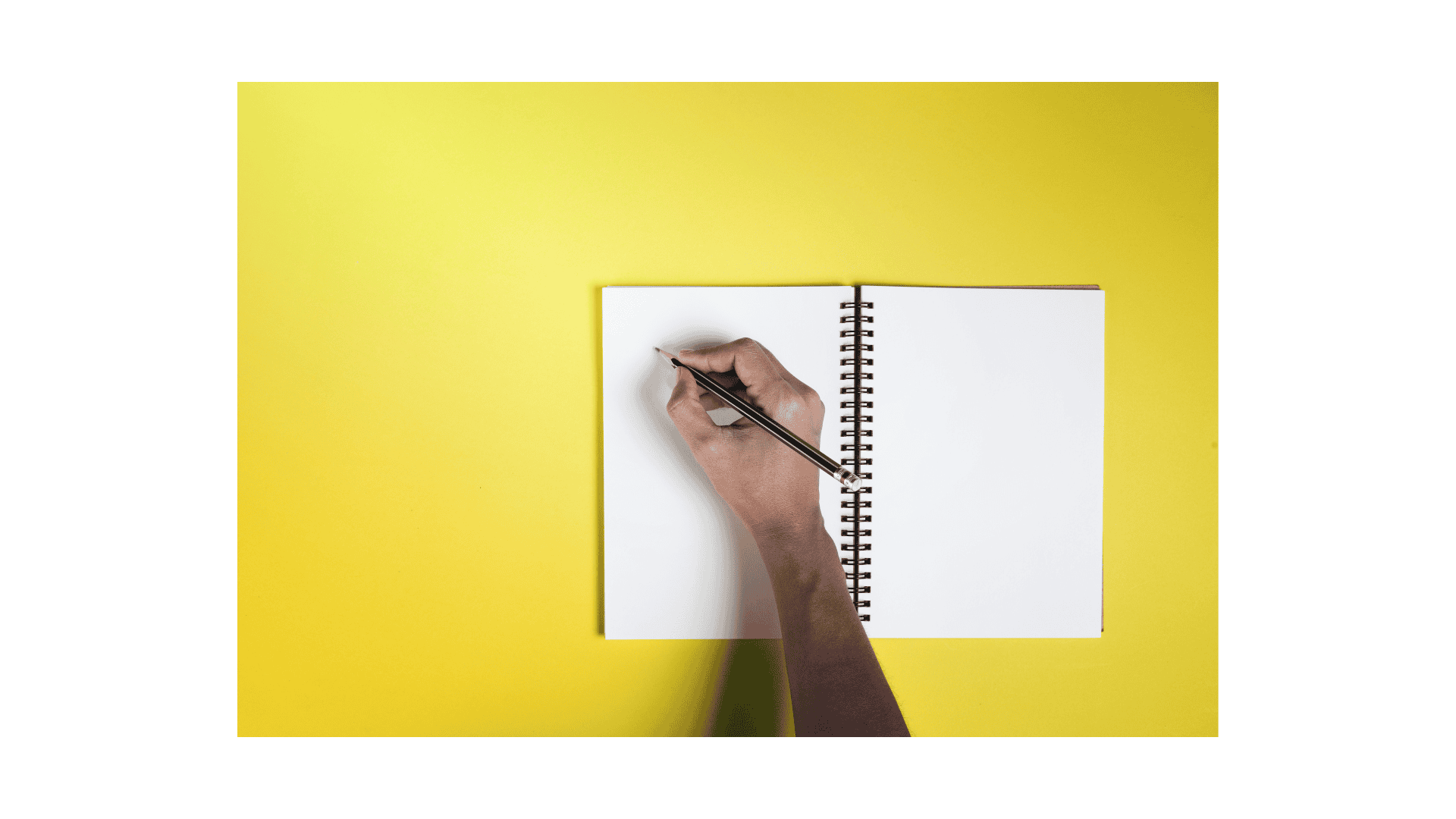A hand holding a pen over a notebook with a yellow background.